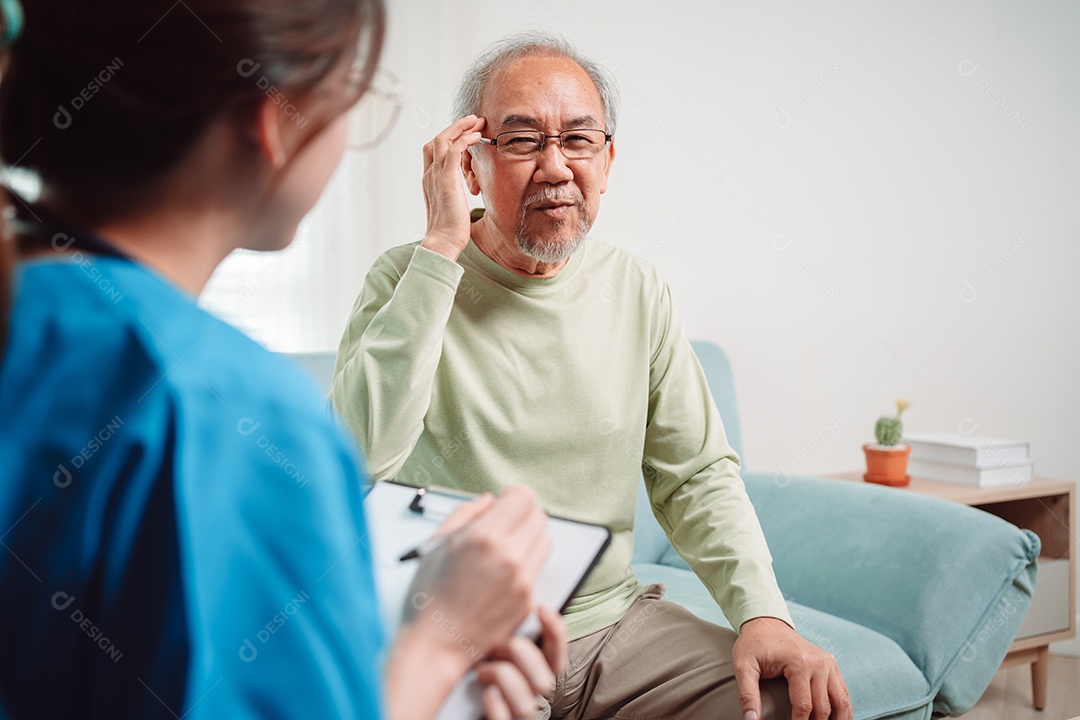 Cuidador asiático falando sobre check-up de paciente masculino sênior na sala de estar em casa.