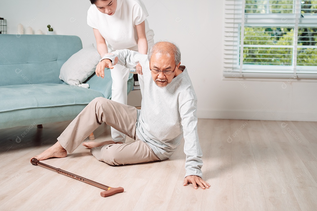 Mulher asiática ajudando o homem sênior que caiu no chão na sala de estar em casa.