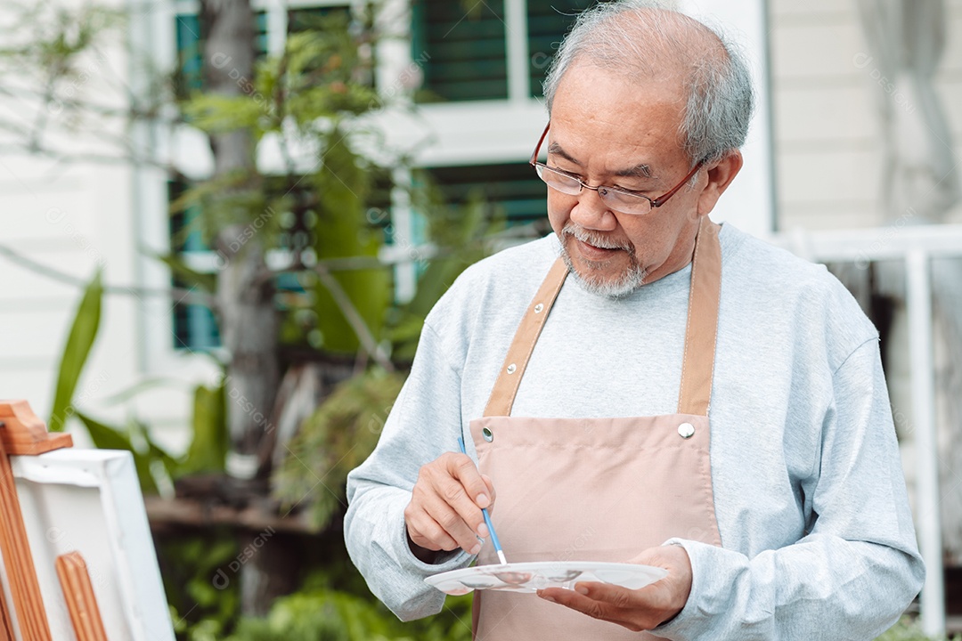 Homem sênior alegre pintando tela no quintal de casa