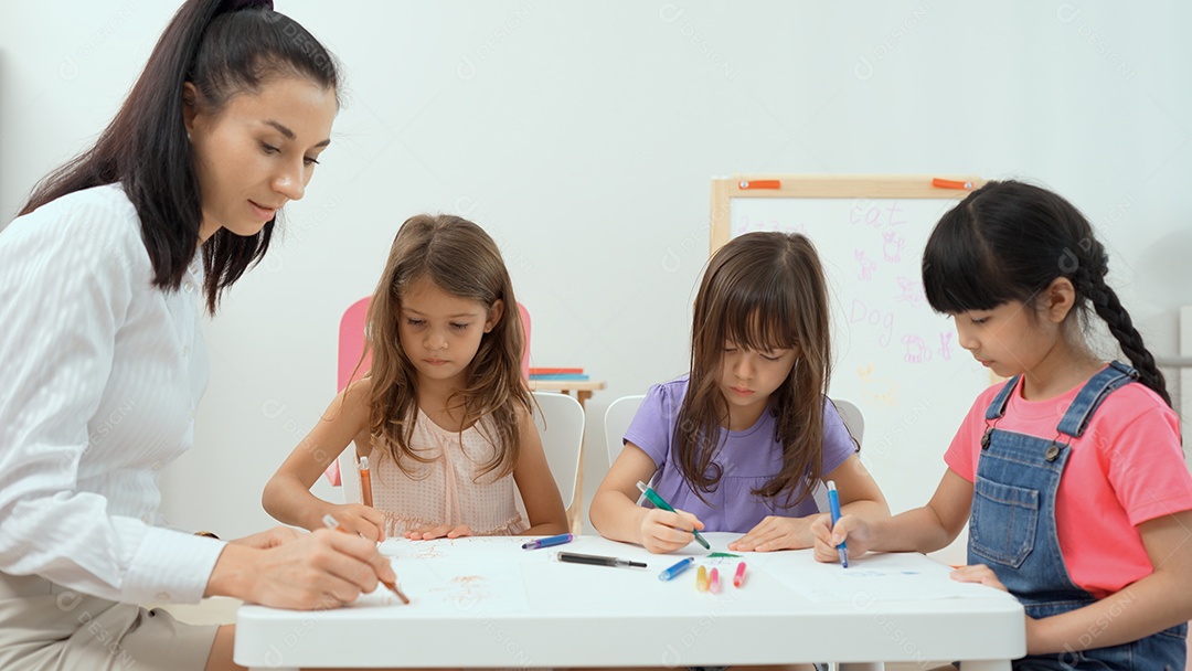 Mulher ensinando menina a pintar livro de cor sobre a mesa em sala de aula, escola de educação infantil.