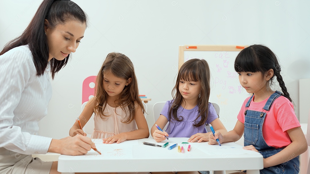 Professora de mulher ensinando menina a pintar livro de cor sobre a mesa em sala de aula