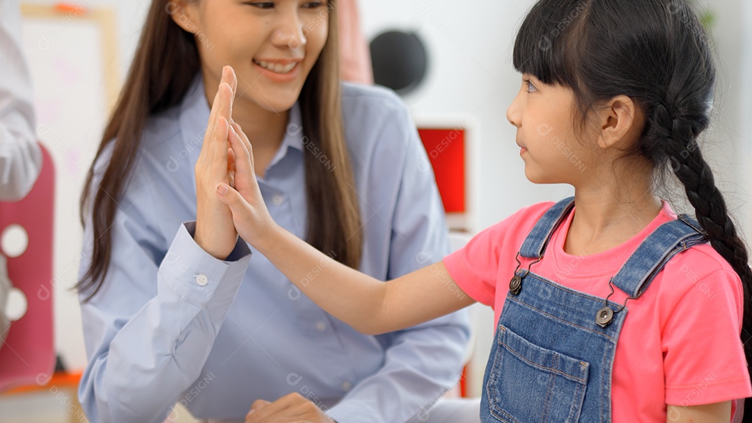Menina asiática termina o livro de cores de tinta sobre a mesa e mais cinco com o professor na sala de aula