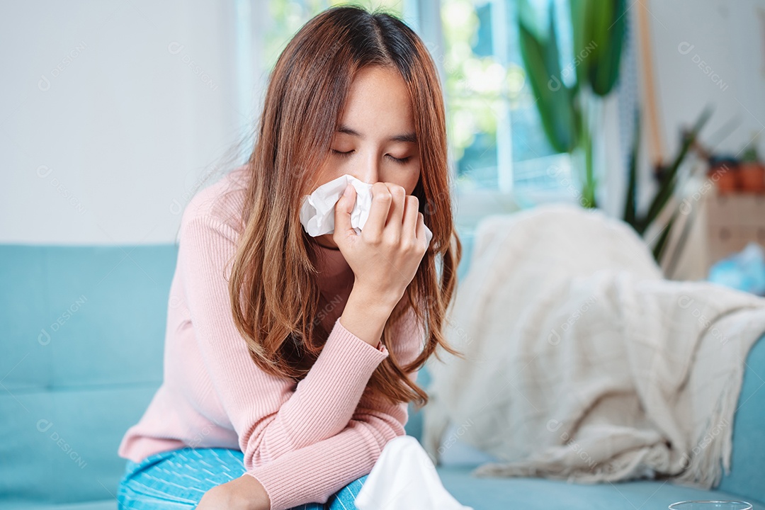 Paciente jovem asiática doente com frio ela espirra com lenço de papel no sofá