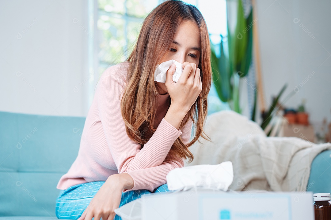 Paciente jovem asiática doente com frio ela espirra com lenço de papel no sofá