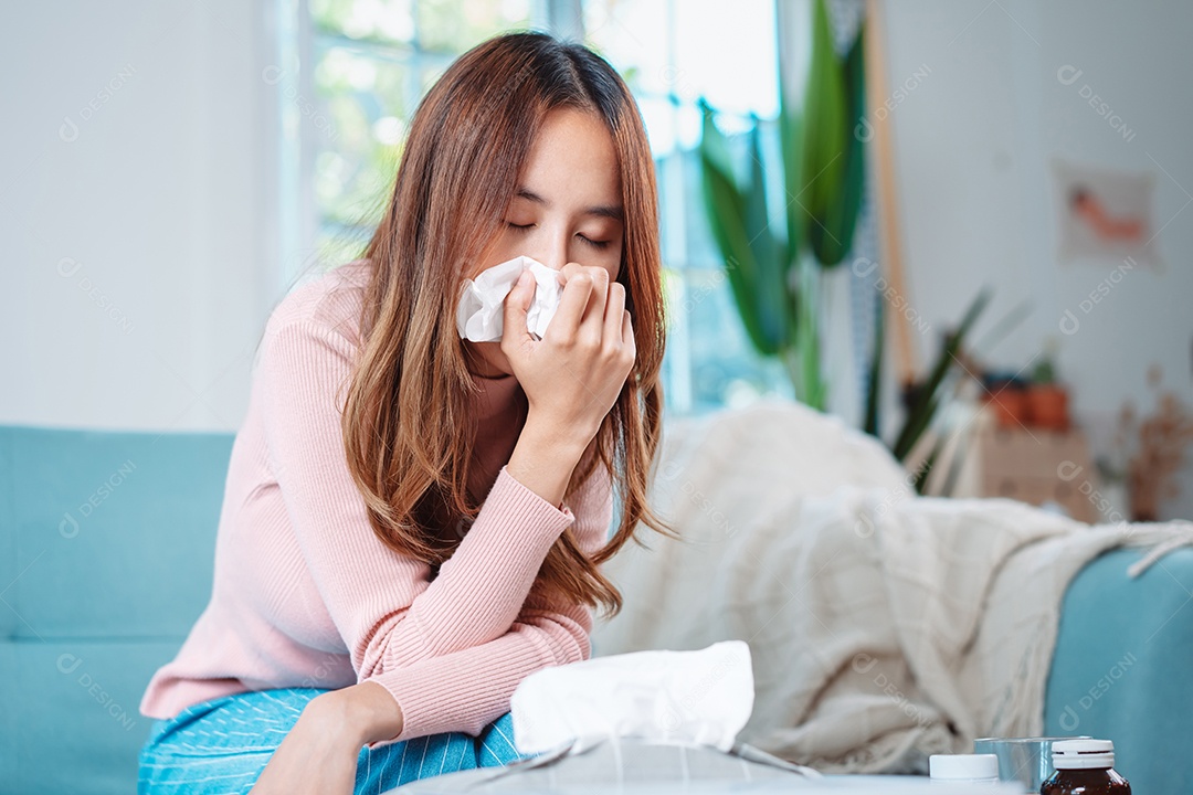 Paciente jovem asiática doente com frio ela espirra com lenço de papel no sofá