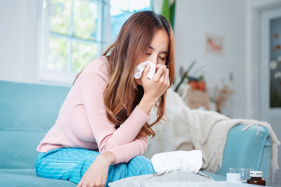 Paciente jovem asiática doente com frio ela espirra com lenço de papel no sofá