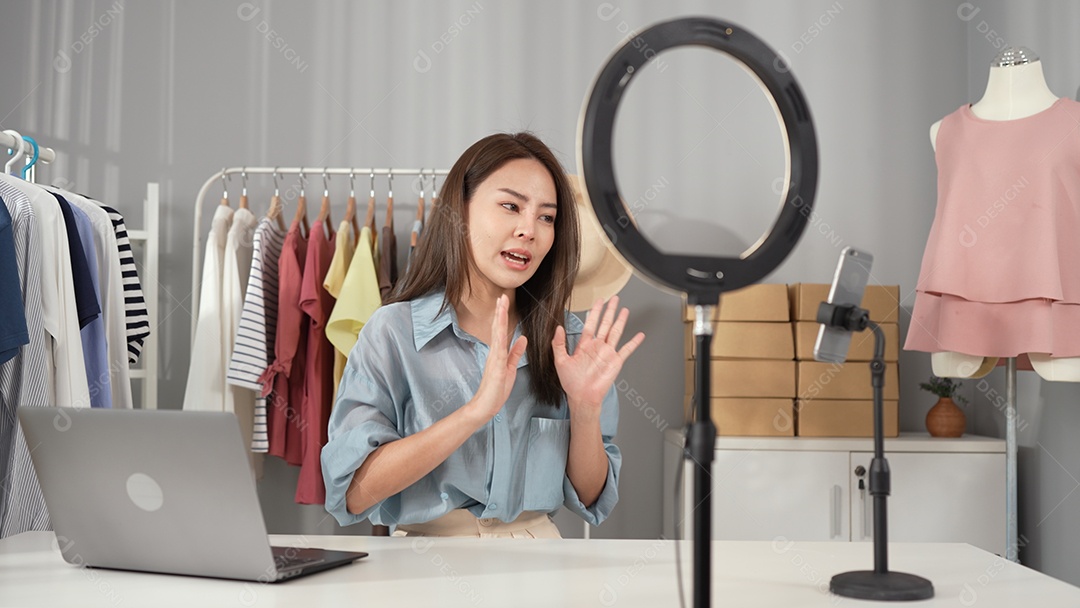 Jovem asiática usa telefone inteligente e fala ao vivo, vende roupas da moda online.