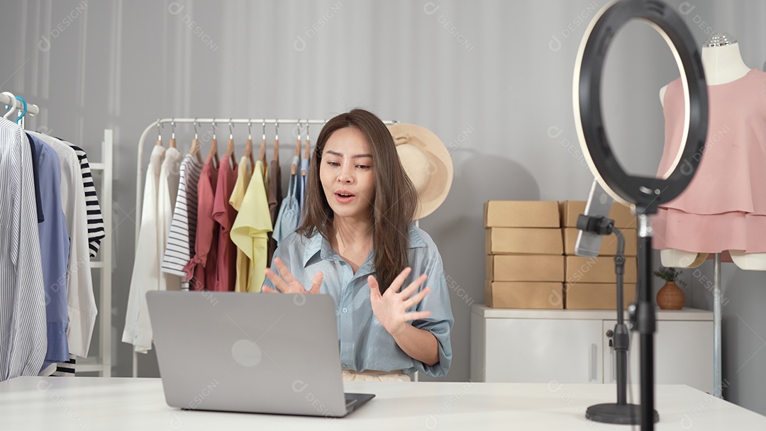 Jovem asiática usa telefone inteligente e fala ao vivo, vende roupas da moda online.