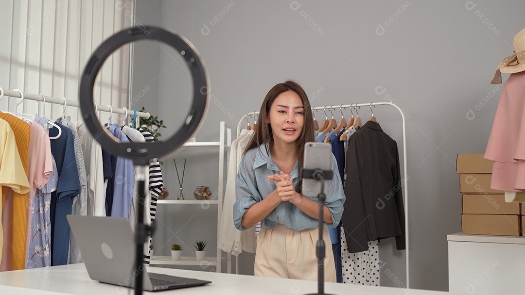 Jovem asiática usa telefone inteligente e fala ao vivo, vende roupas da moda online.