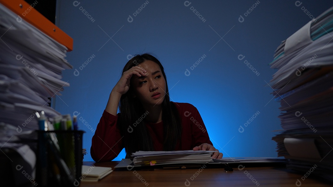 Estressada jovem asiática sentada trabalhando horas extras fazendo negócios tardios no escritório à noite