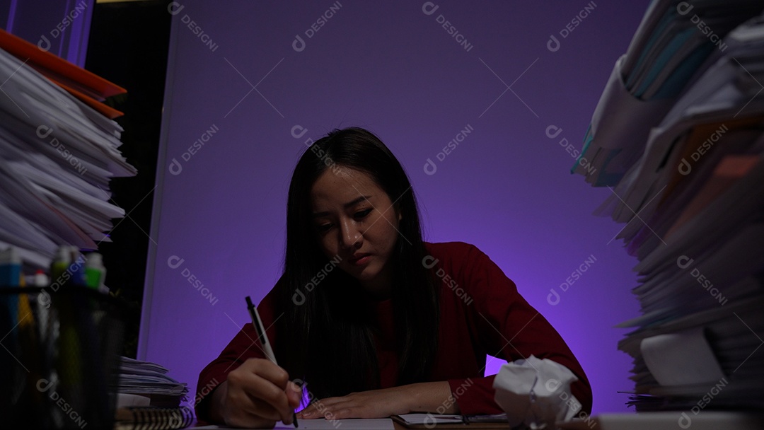 Estressada jovem asiática sentada trabalhando horas extras fazendo negócios tardios no escritório à noite
