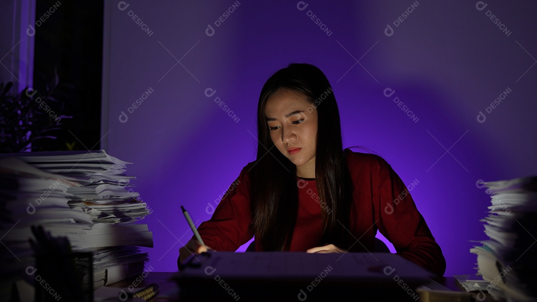 Estressada jovem asiática sentada trabalhando horas extras fazendo negócios tardios no escritório à noite