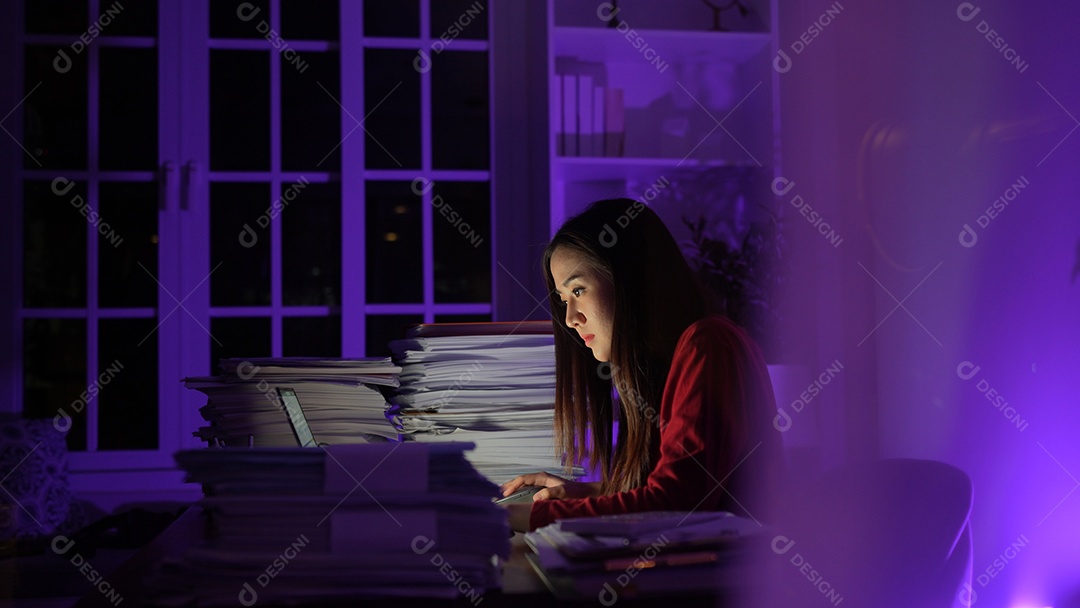 Jovem asiática sentada trabalhando horas extras fazendo negócios tardios no escritório à noite