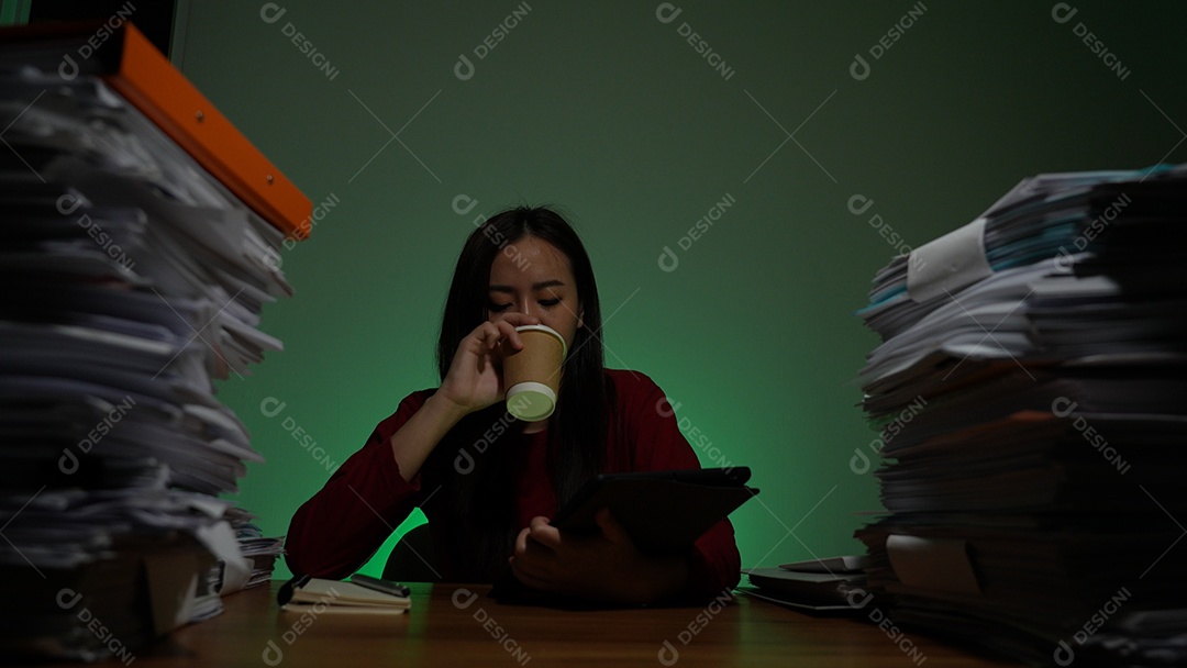 Jovem asiática sentada trabalhando horas extras fazendo negócios tardios no escritório à noite