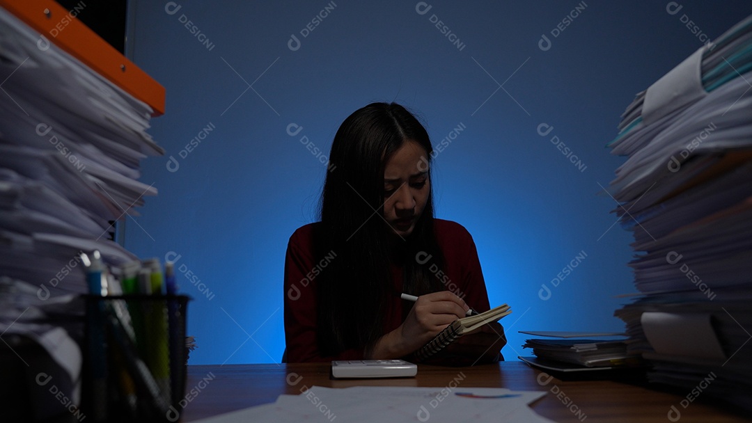 Jovem asiática sentada trabalhando horas extras fazendo negócios tardios no escritório à noite