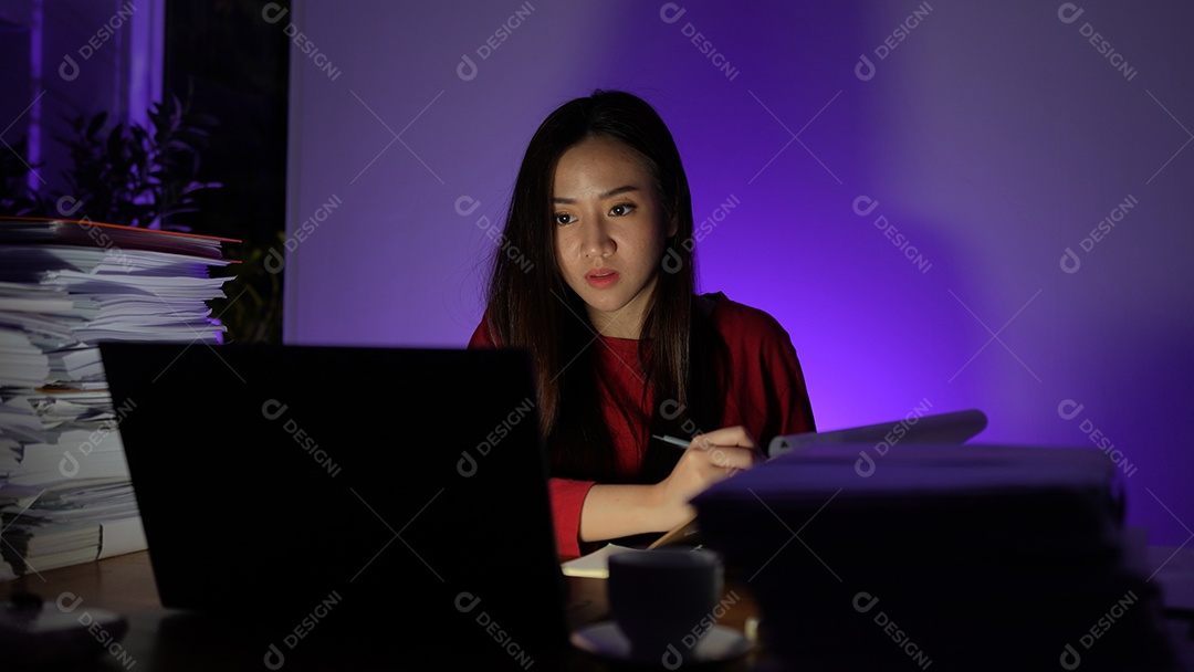 Jovem asiática sentada trabalhando horas extras fazendo negócios tardios no escritório à noite
