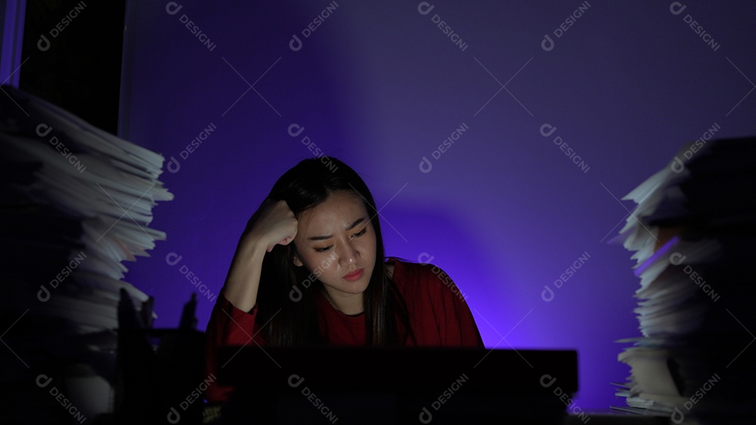 Jovem asiática sentada trabalhando horas extras fazendo negócios tardios no escritório à noite