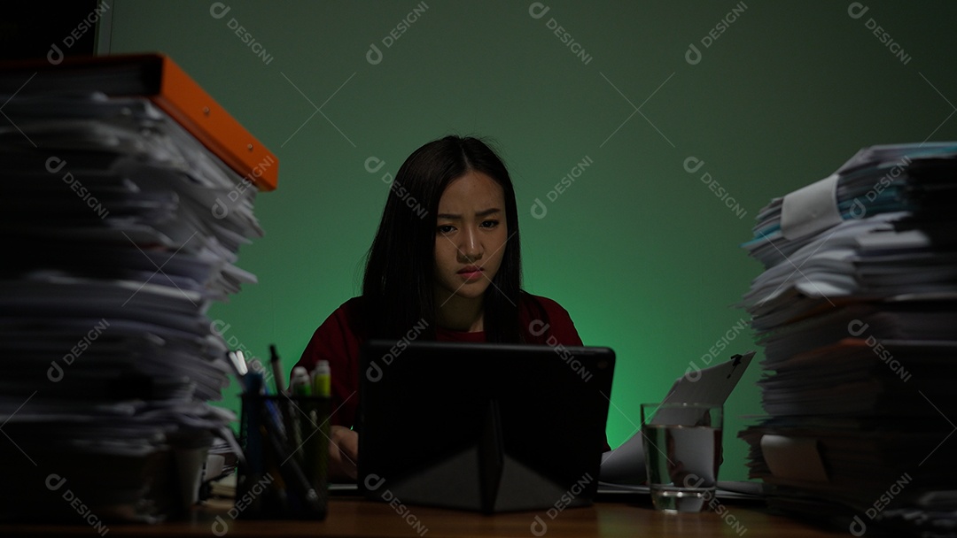 Jovem asiática sentada trabalhando horas extras fazendo negócios tardios no escritório à noite
