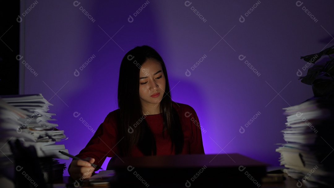Jovem asiática sentada trabalhando horas extras fazendo negócios tardios no escritório à noite