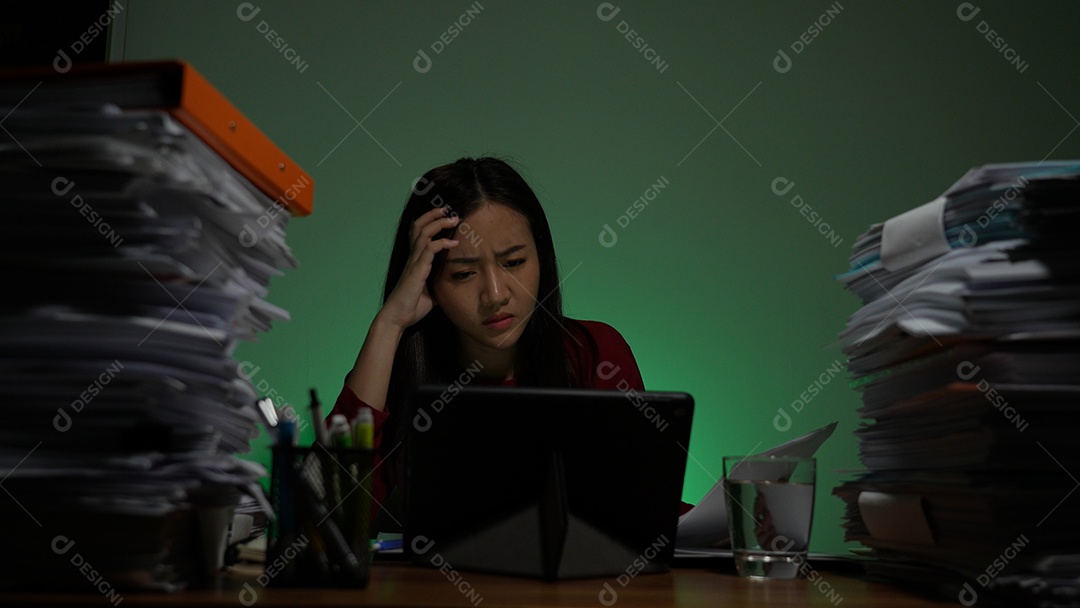 Jovem asiática sentada trabalhando horas extras fazendo negócios tardios no escritório à noite