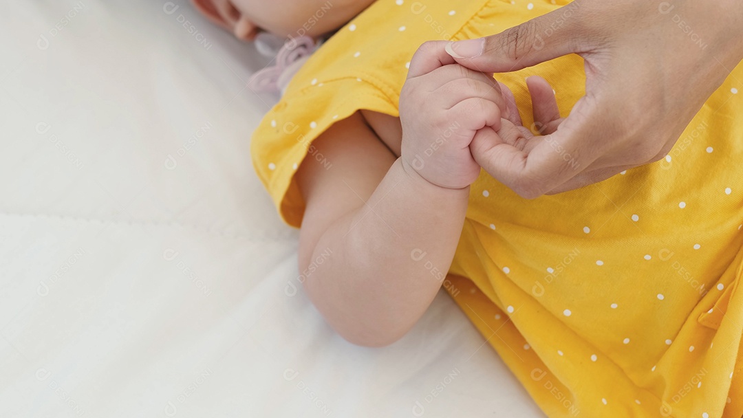 Mãe asiática segurando a mão de seu bebê recém-nascido na cama de manhã