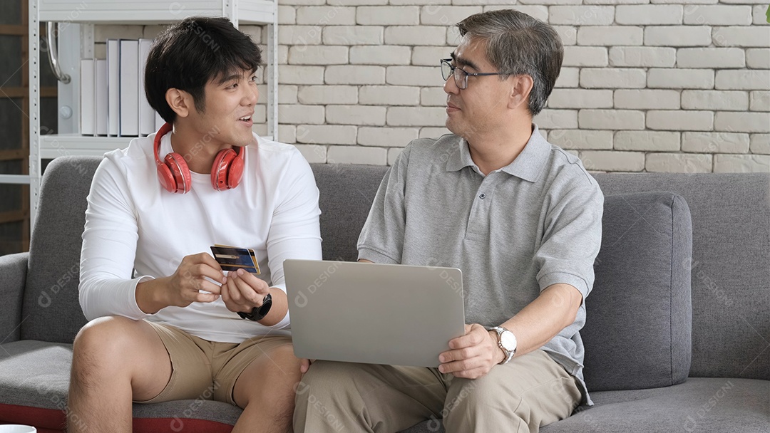 O pai sênior asiático e o filho adulto passam tempo juntos com o laptop em casa.