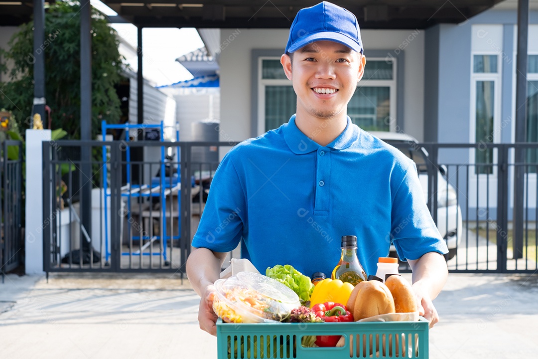 O homem asiático de entrega de comida em uniforme azul dá frutas e vegetais para a casa da frente do cliente recepto