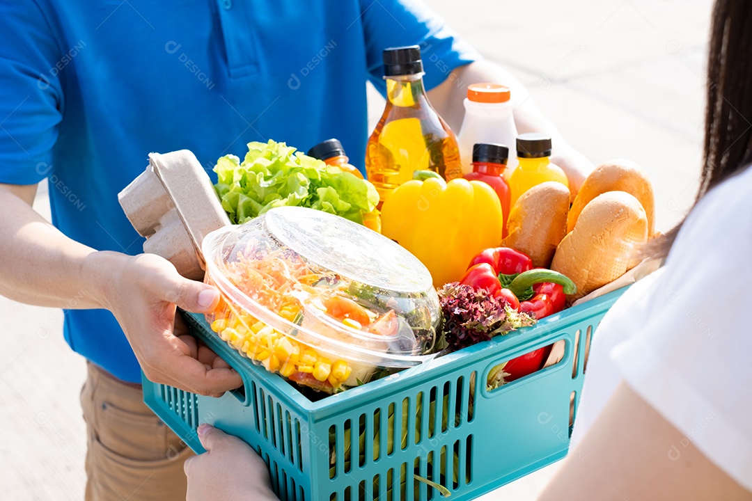 O homem asiático de entrega de comida em uniforme azul dá frutas e vegetais para a casa da frente do cliente recepto