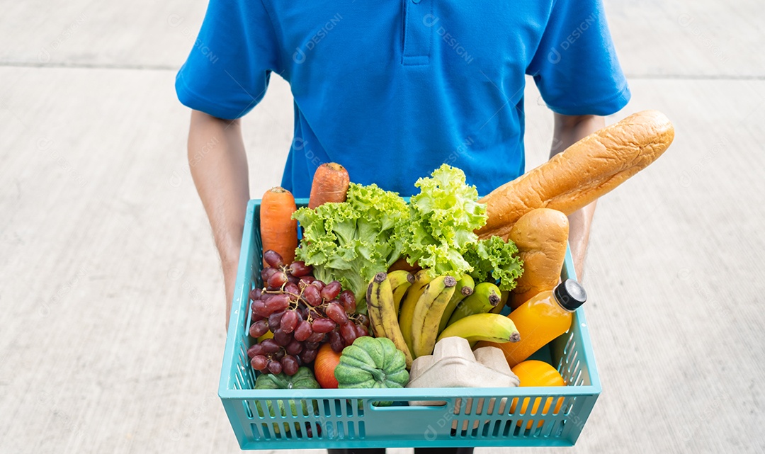 O homem asiático de entrega de comida em uniforme azul dá frutas e vegetais para a casa da frente do cliente receptor