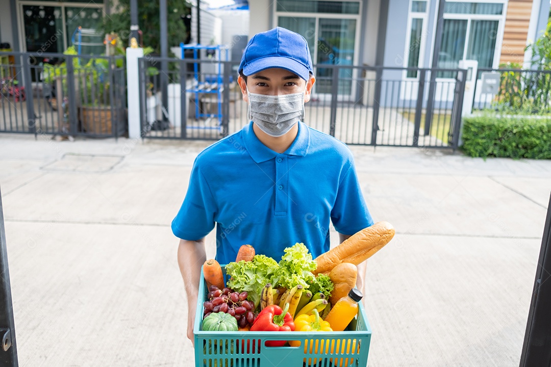 Entrega de comida Homem asiático usando máscara de uniforme dá frutas e vegetais para a casa da frente do cliente receptor