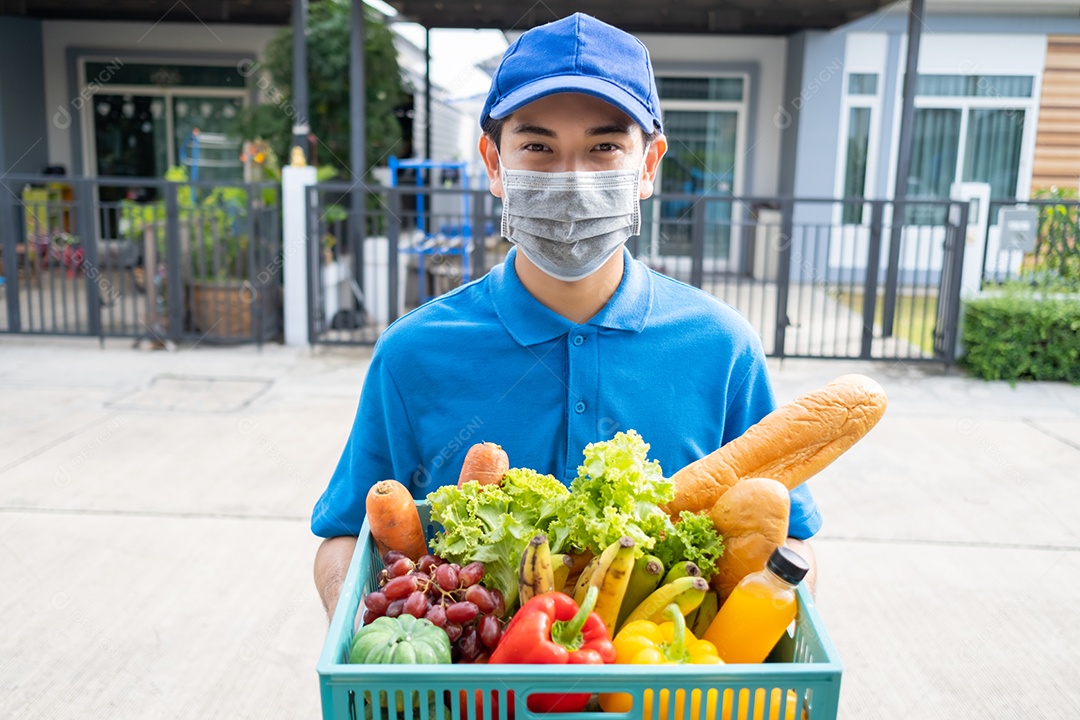 Entrega de comida Homem asiático usando máscara de uniforme dá frutas e vegetais para a casa da frente do cliente receptor