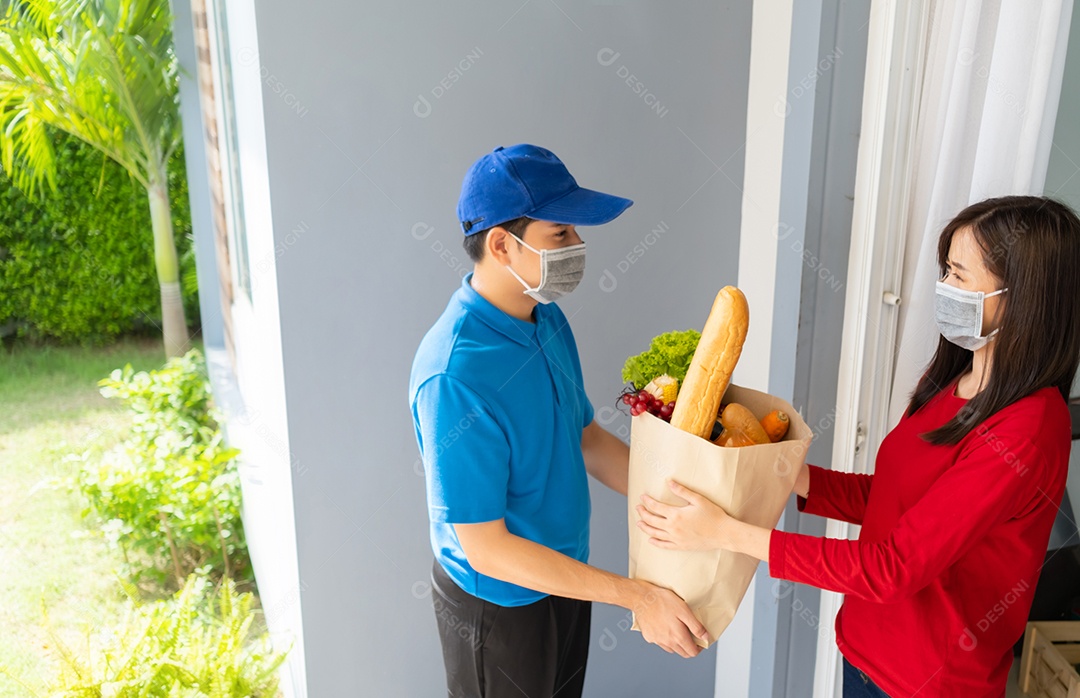O homem asiático de entrega de comida em uniforme azul dá frutas e vegetais para a casa da frente do cliente receptor