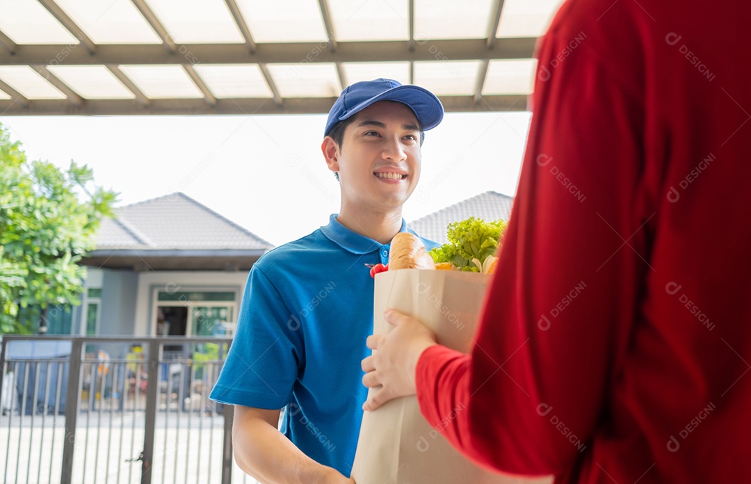 O homem asiático de entrega de comida em uniforme azul dá frutas e vegetais para a casa da frente do cliente receptor