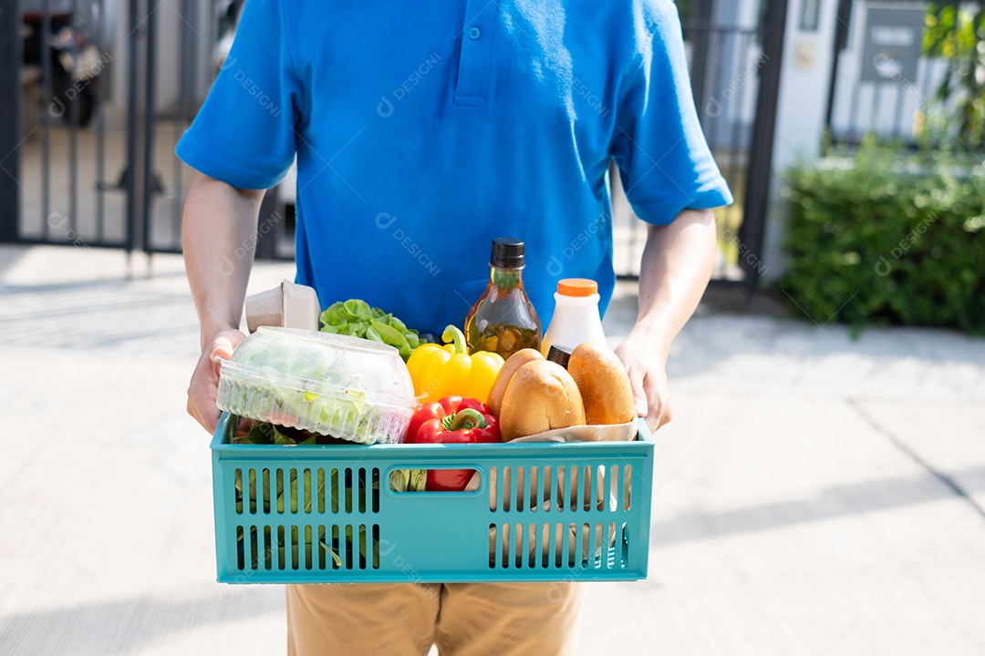 Homem asiático de entrega de comida em uniforme dá frutas e vegetais para a casa da frente do cliente receptor