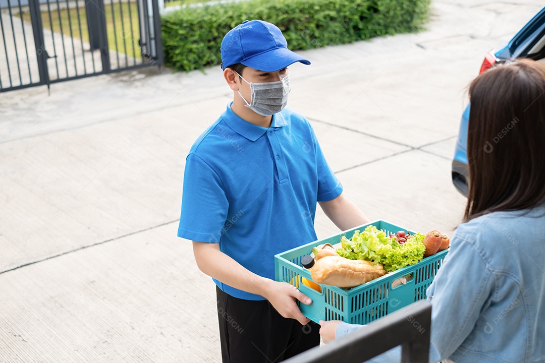 O homem asiático de entrega de comida em uniforme azul dá frutas e vegetais para a casa da frente do cliente receptor