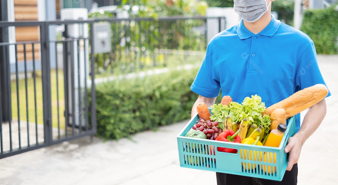 O homem asiático de entrega de comida em uniforme azul dá frutas e vegetais para a casa da frente do cliente receptor