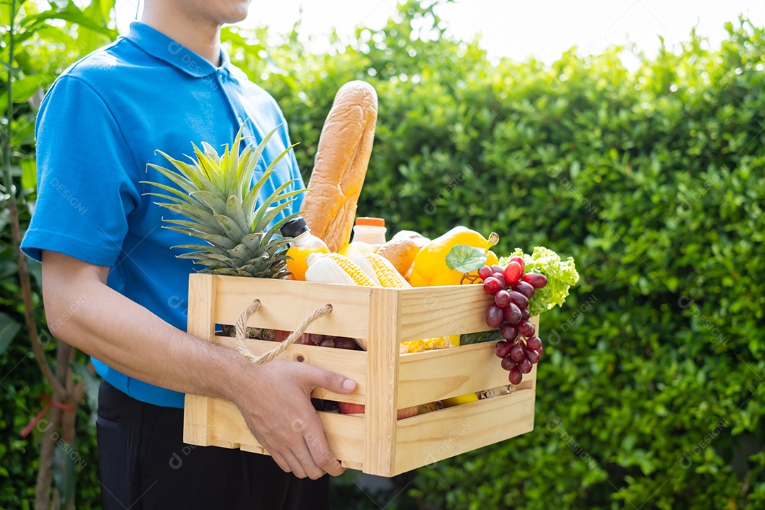O homem asiático de entrega de comida em uniforme azul dá frutas e vegetais para a casa da frente do cliente receptor