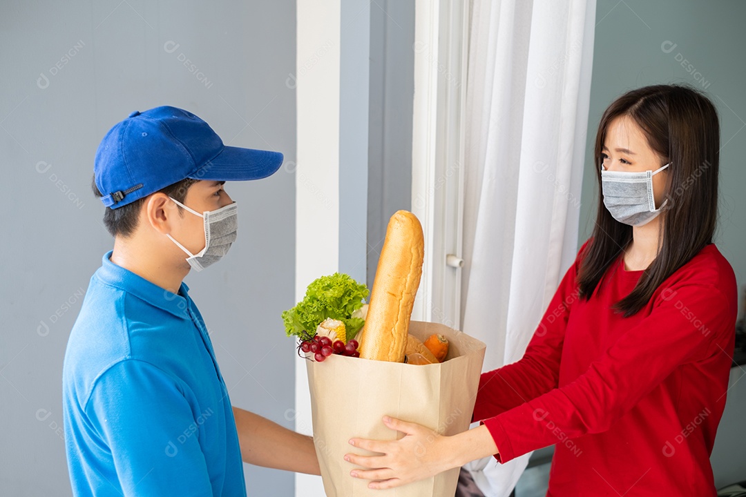 O homem asiático de entrega de comida em uniforme azul dá frutas e vegetais para a casa da frente do cliente receptor