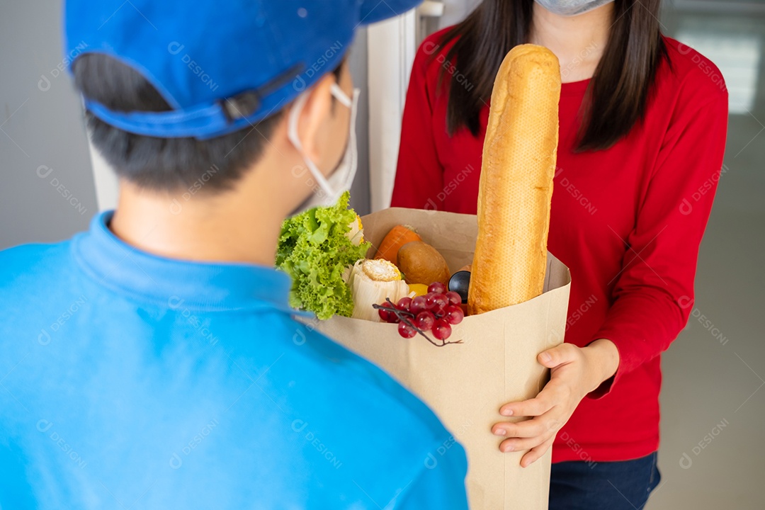 O entregador de comida usando máscara dá supermercado de compras de frutas e vegetais para a casa da frente do cliente