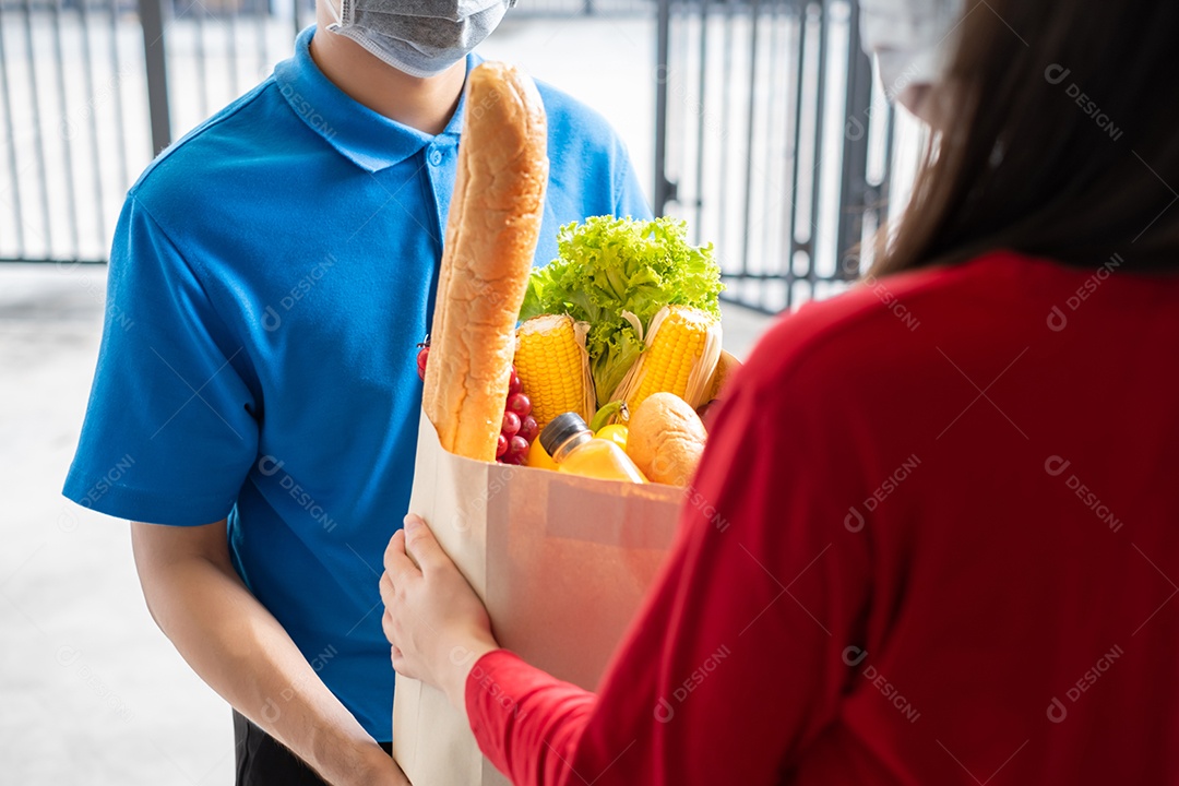 O entregador de comida usando máscara dá supermercado de compras de frutas e vegetais para a casa da frente do cliente