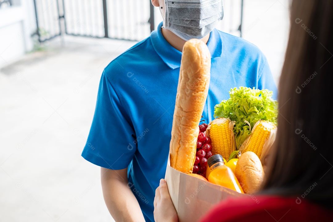 O entregador de comida usando máscara dá supermercado de compras de frutas e vegetais para a casa da frente do cliente