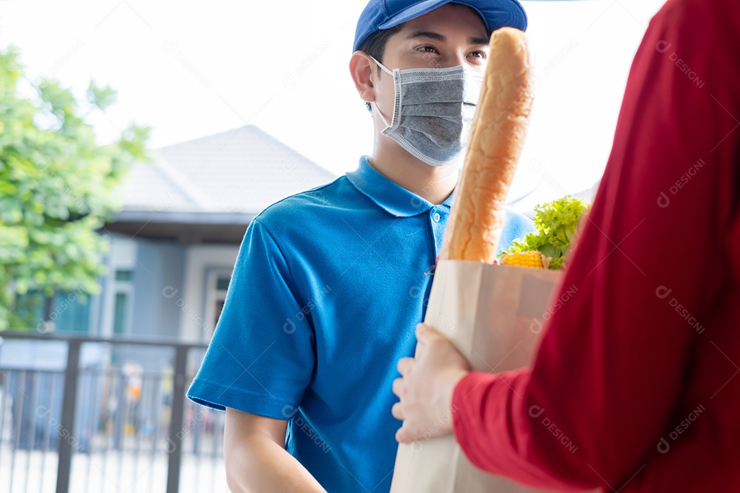 O entregador de comida usando máscara dá supermercado de compras de frutas e vegetais para a casa da frente do cliente