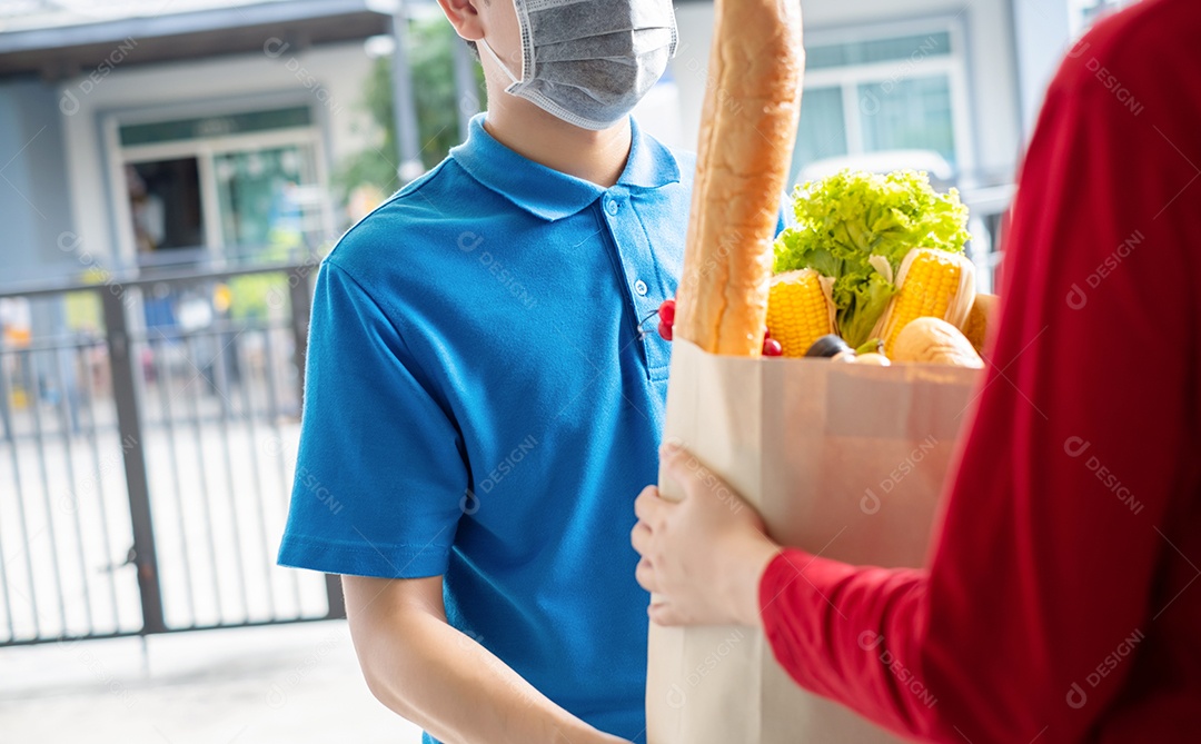 O entregador de comida usando máscara dá supermercado de compras de frutas e vegetais para a casa da frente do cliente