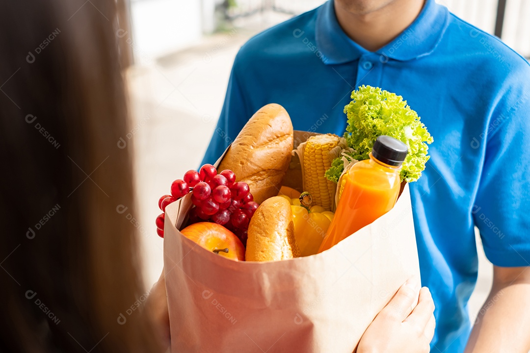 O entregador de comida usando máscara dá supermercado de compras de frutas e vegetais para a casa da frente do cliente