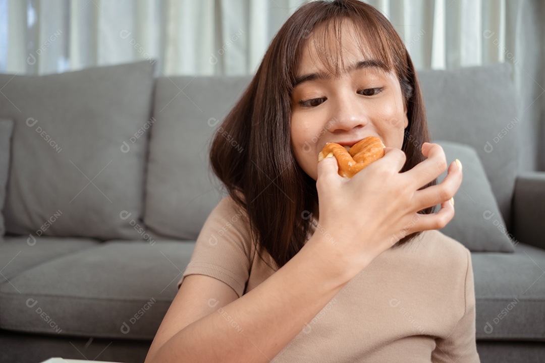 Jovem mulher asiática comendo rosquinha na sala de estar