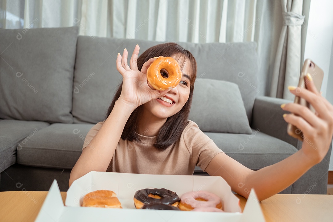 Jovem mulher asiática comendo rosquinha na sala de estar