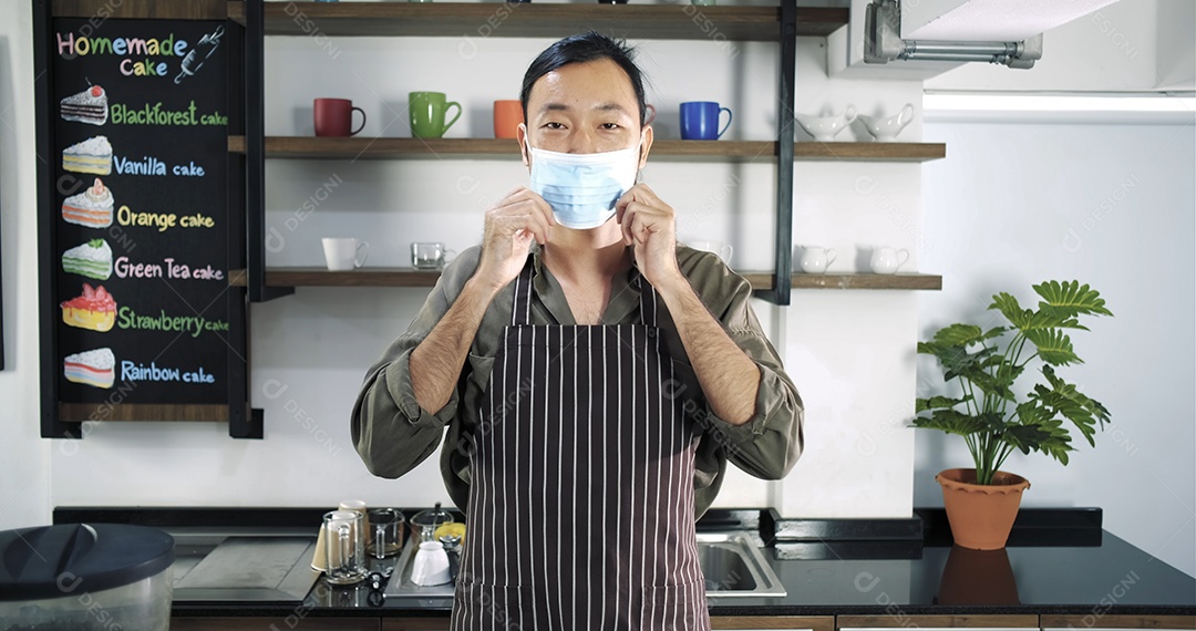 Barista bonito com máscara médica e avental em pé no bar do café moderno.