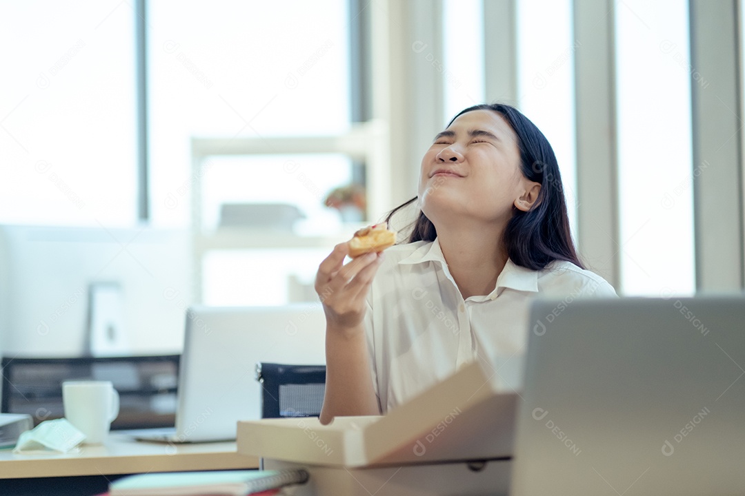 Mulher de negócios sentada na cadeira comendo pizza no almoço enquanto trabalha