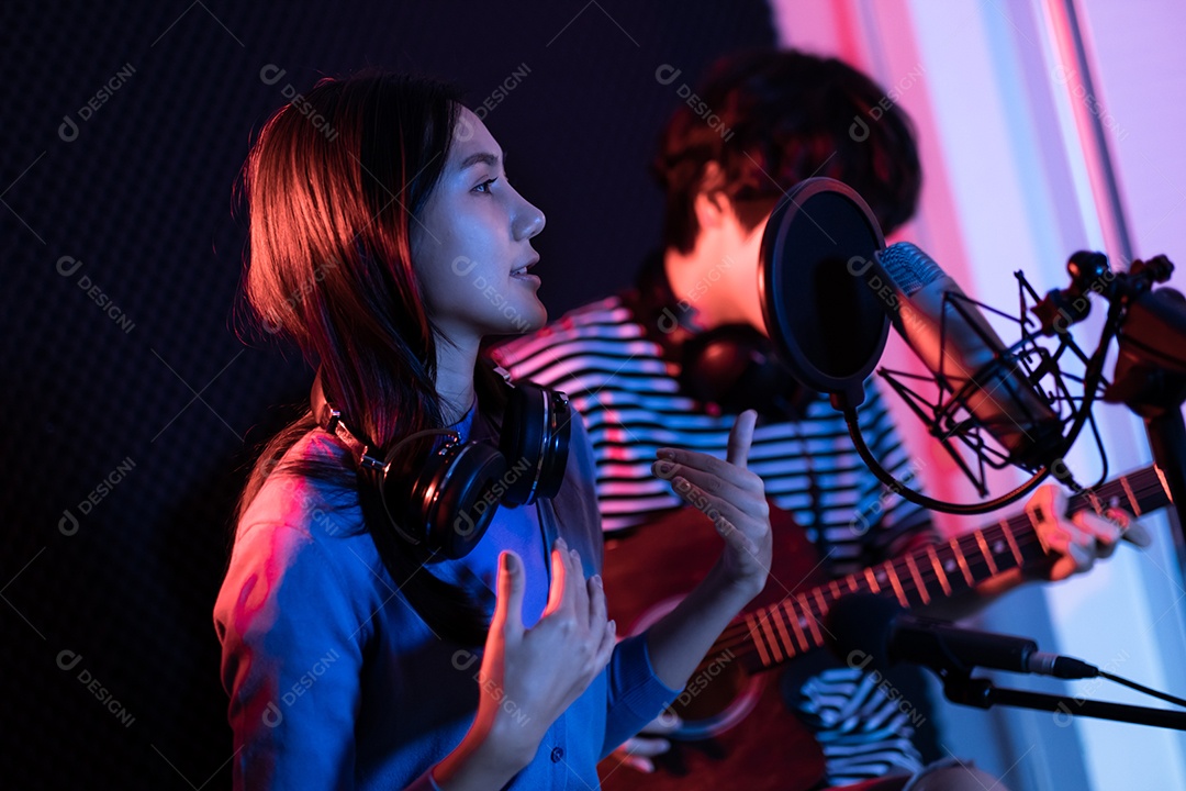 Jovem mulher asiática cantando enquanto homem no fundo tocando violão.