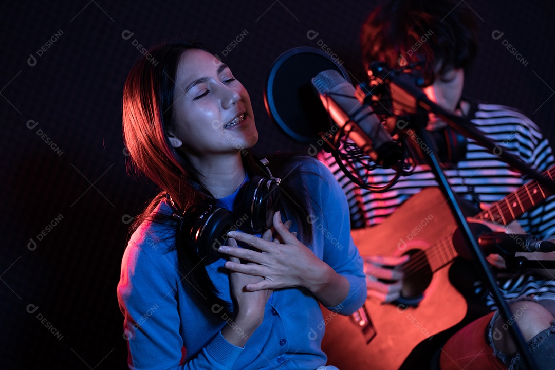 Jovem mulher asiática cantando enquanto homem no fundo tocando violão.